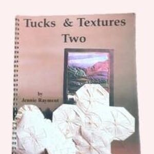 May include: A spiral-bound instructional book titled Tucks & Textures Two by Jennie Rayment. The cover features a landscape image and several white fabric samples with intricate folded tucks and stitched textures arranged in the foreground.