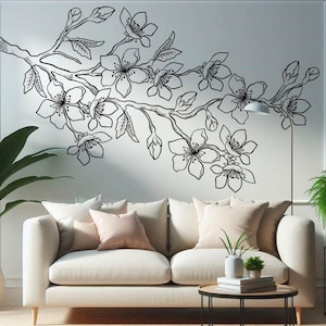 May include: A white sofa with pillows in a living room setting. A black and white floral wall decal is on the wall behind the sofa. A small black table with a plant and books is in front of the sofa.