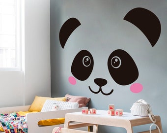 May include: A white and black panda face wall decal with pink cheeks, above a wooden table and chair set in a child's bedroom.