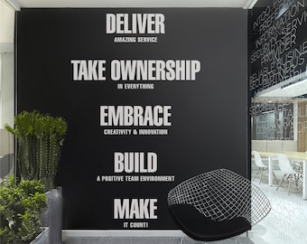 May include: A black wall with white text that reads "DELIVER AMAZING SERVICE", "TAKE OWNERSHIP IN EVERYTHING", "EMBRACE CREATIVITY & INNOVATION", "BUILD A POSITIVE TEAM ENVIRONMENT", and "MAKE IT COUNT!". A black chair and potted plants are in front of the wall.