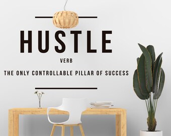 Può includere: Un muro bianco con una citazione motivazionale in bianco e nero che recita "Hustle Verb The Only Controllable Pillar of Success". In primo piano, un tavolo di legno con una sedia bianca e una pianta in vaso.
