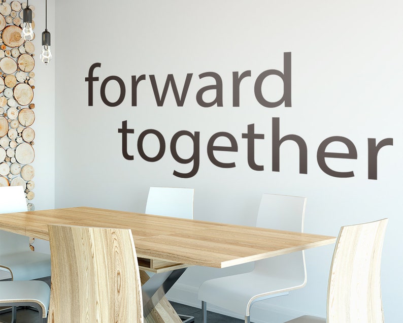 May include: A wooden table with white chairs in a room with a white wall. The wall has the words "forward together" written on it in black.