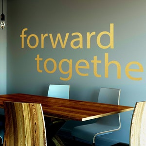 May include: A wooden table with four chairs in a room with a light grey wall. The wall has the words "forward together" written on it in gold lettering.