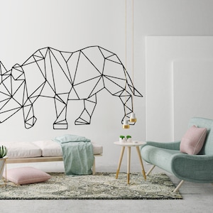 Puede incluir: Arte de pared de rinoceronte negro geométrico sobre un fondo blanco. El rinoceronte está en un salón con un sofá azul claro, una mesa de café blanca y una manta de tiro verde claro en una cama de día blanca.