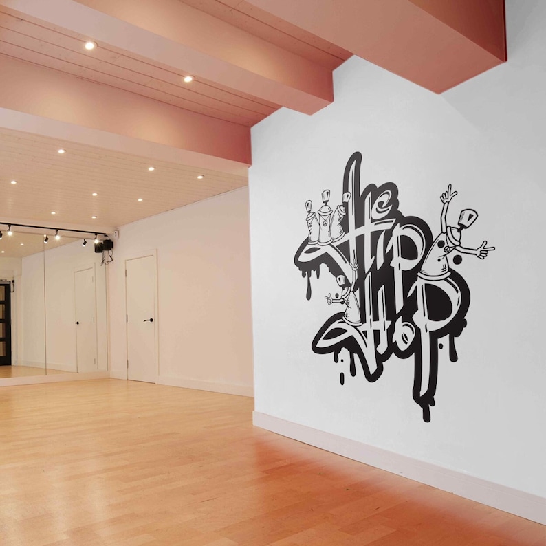 K&ouml;nnte beinhalten: Eine wei&szlig;e Wand mit einem schwarzen und wei&szlig;en Graffiti-Design, auf dem "The Hip Hop" mit Spraydosen und einer Comicfigur steht.