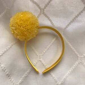 Bright yellow pom pom on matching yellow satin-covered headband