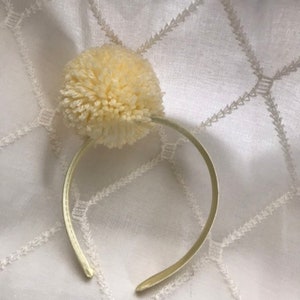 Big cream colored pom on coordinating satin cream colored headband