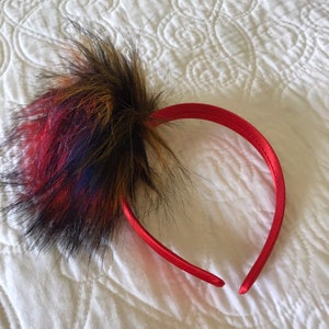 May include: A red satin headband with a multi-colored faux fur pom-pom.