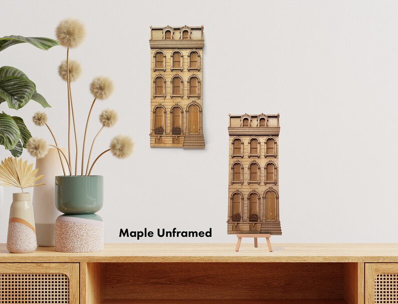 May include: Two wooden wall decor pieces in the shape of a brown townhouse with multiple windows. The smaller piece is on a wooden easel and the larger piece is on a white wall. The text "Maple Unframed" is below the pieces.