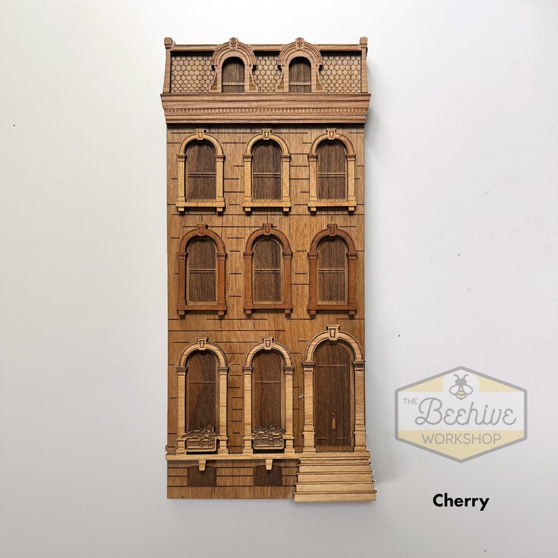May include: A wooden model of a three-story townhouse with a detailed facade, featuring windows, a door, and a small stoop. The model is made of cherry wood and is laser cut. The Beehive Workshop logo is visible in the bottom right corner.