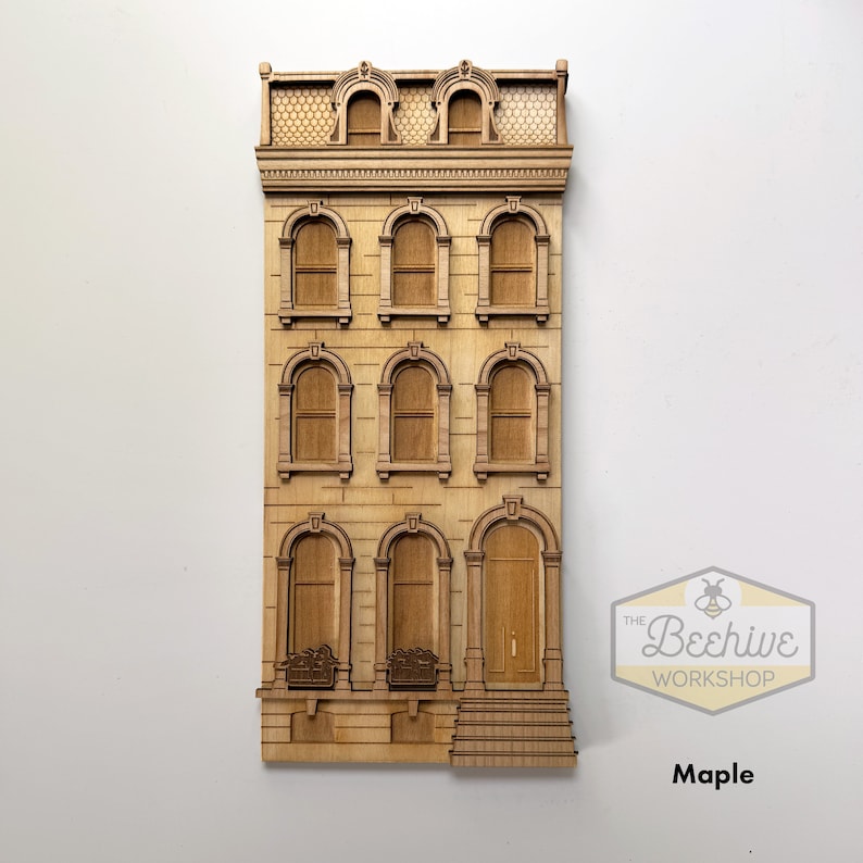 May include: A wooden cutout of a brown three-story building with arched windows and a door. The building has a detailed facade with decorative trim. The cutout is made of maple wood and is part of The Beehive Workshop.