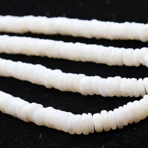 May include: A white shell necklace made of small, round, flat beads. The necklace is layered and appears to be made of natural materials.