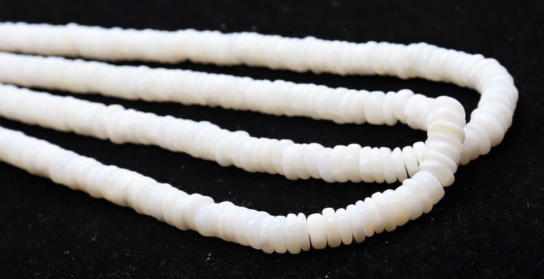 May include: A white shell necklace made of small, round, flat beads. The necklace is layered and appears to be made of natural materials.