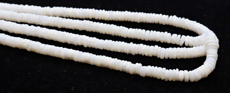 May include: A strand of white, opaque, round beads, strung together to form a necklace. The beads are slightly irregular in shape and have a matte finish.