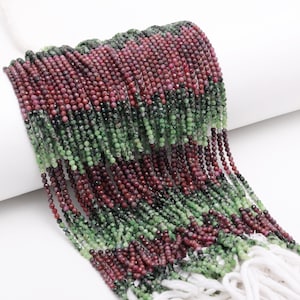 Peut inclure: Un brin de perles de pierres précieuses vertes et rouges. Les perles sont petites et rondes, et elles sont enfilées sur un fil blanc. Les perles sont disposées de manière aléatoire.