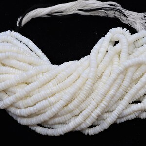 May include: A strand of white shell beads, each bead is a small, flat disc with a slightly raised center. The beads are strung together on a white cord.