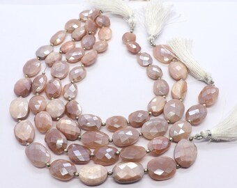 May include: A strand of pink moonstone beads with a faceted oval shape. The beads are strung on a silver wire and have a white tassel at each end.