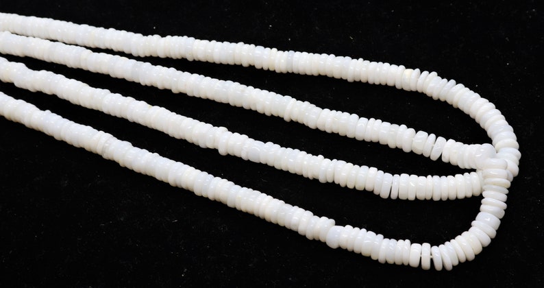 May include: A strand of white shell beads, with a smooth, polished finish. The beads are arranged in a long, continuous string, and they are all of a uniform size and shape.