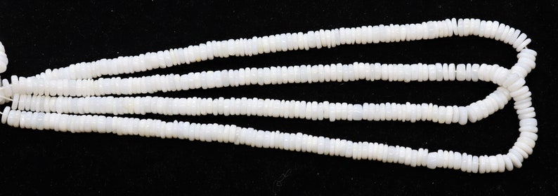 May include: A strand of white shell beads, with a smooth, matte finish. The beads are oval shaped and have a slightly irregular texture. The strand is approximately 18 inches long.