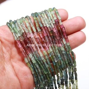 Op de afbeelding: Een streng multi-kleurige toermalijn kralen, met tinten groen, roze en blauw. De kralen zijn gefacetteerd en hebben een rechthoekige vorm. De kralen zijn geregen op een doorzichtige draad en zijn klaar om te worden gebruikt voor het maken van sieraden.