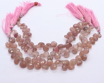 May include: A strand of pink gemstone beads with a faceted, teardrop shape. The beads are strung on a cord with pink tassels at each end.