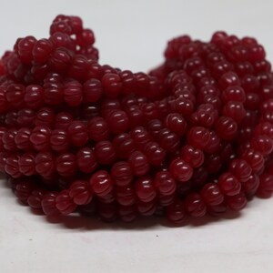 May include: A strand of deep red, faceted, pumpkin-shaped beads. The beads are strung together on a clear thread.