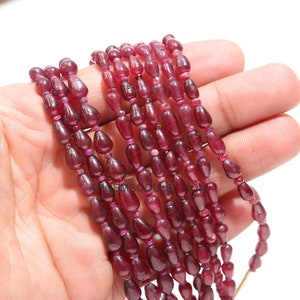 May include: A strand of deep red ruby gemstone beads in a teardrop shape. The beads are strung on a thin wire and are approximately 6mm in size.
