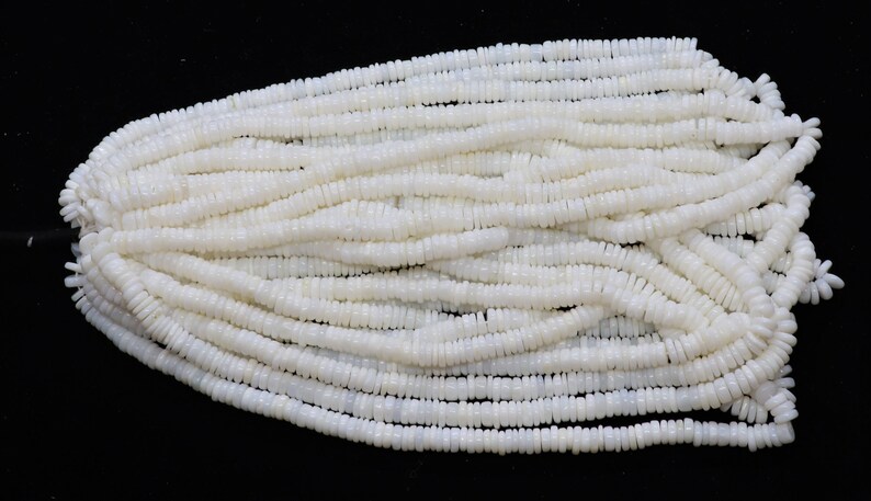 May include: A strand of white shell beads, each bead is a small, flat disc with a slightly rounded edge.