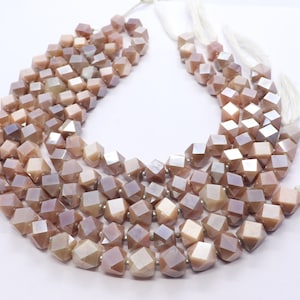 May include: A strand of iridescent sunstone beads, each bead is faceted and shaped like a cube. The beads are strung on a white cord and are a light pink color.