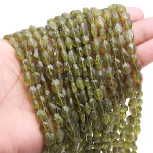 以下が含まれることがあります： 面取りされた楕円形の緑色の宝石ビーズのストランド。ビーズは透明な糸に通されており、ジュエリー作りに使用できます。