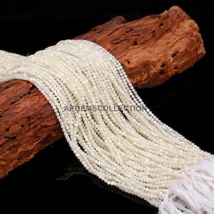 May include: A collection of small, off-white beads, possibly pearls or gemstones, are arranged over a piece of weathered wood. The beads are tightly strung, creating a flowing, textured appearance. The text "APORMSCOLLECTION" is visible. The background is black.