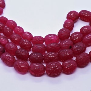 Op de afbeelding: Een streng roze ovale kralen met gegraveerde bloemmotieven. De kralen zijn geregen aan een rood koord.