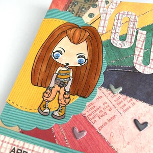 May include: A colorful card with a cartoon girl wearing a yellow and black striped shirt and blue jeans. The card says "You are beautiful" and has a heart design.