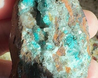May include: A rough-hewn rock fragment with a mix of colors. The stone features patches of vibrant turquoise, interspersed with areas of brown, orange, and white. The texture appears crystalline and porous, suggesting a mineral specimen.
