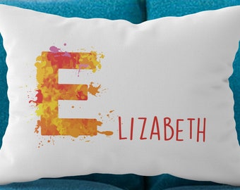 May include: A rectangular white throw pillow featuring a large, stylized letter E with a watercolor-style orange, yellow, and red paint splatter effect. To the right of the letter E, the text LIZABETH is printed in a simple red sans-serif font.