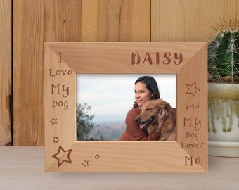 May include: A light-colored wooden picture frame with the words "I Love My dog" and "and My dog Loves Me" engraved on the frame. The name "Daisy" is engraved at the top. The frame holds a photo of a woman and a golden retriever.