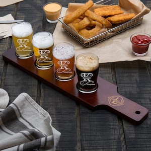 May include: A wooden beer flight paddle with four glasses. The glasses are filled with different types of beer and are engraved with the name "Kenneth Kaufman".