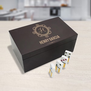May include: A dark brown wooden box with a gold engraved monogram and the name "HENRY GARCIA". The box is open and there are five white dominoes with black dots on them.