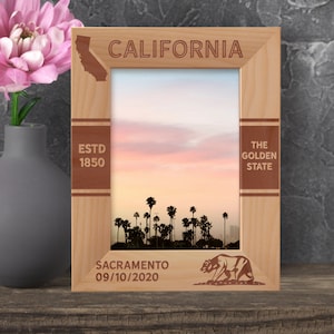 May include: A wooden picture frame with a sunset photo of palm trees. The frame is engraved with the words "California", "The Golden State", "Est. 1850", "Sacramento 09/10/2020", and a silhouette of a bear.