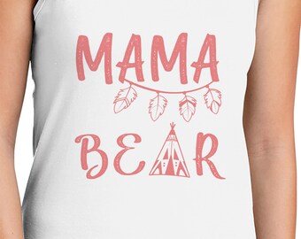 May include: White tank top with the words "MAMA BEAR" in pink script. The word "MAMA" is above a string of feathers, and "BEAR" is below a teepee graphic. The design is centered on the front of the shirt.
