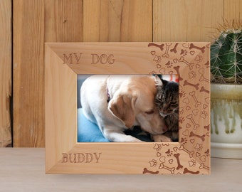 May include: A wooden photo frame with a light brown finish. The frame has a cutout design of paw prints, hearts, and bones. The text "MY DOG BUDDY" is engraved on the frame. A photo of a dog and cat is inside the frame.