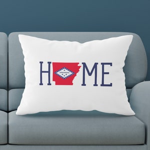 May include: White pillow with the word "HOME" in blue lettering. The "O" is replaced with the outline of the state of Arkansas in red with the state flag inside.