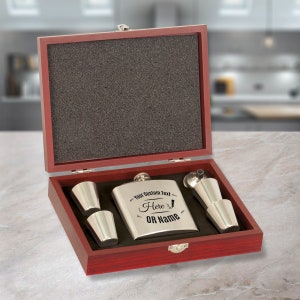 May include: A wooden box with a red finish contains a stainless steel flask, two shot glasses, and a funnel. The flask is engraved with the text "Your Custom Text Here OR Name".