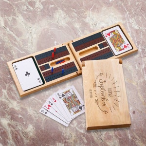 May include: A wooden cribbage board game set with a personalized wooden box. The box has the text "Thomas September 4 09.01.1983" engraved on it. The cribbage board is open and shows the playing surface with pegs and cards.