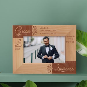 May include: A wooden picture frame with a brown and natural wood finish. The frame has a cutout design with the word "Groom" and the date "12 25 2021". The frame also has the text "Love is composed of a single soul inhabiting two bodies." and the name "Lawrence". A photo of a man in a suit is in the frame.