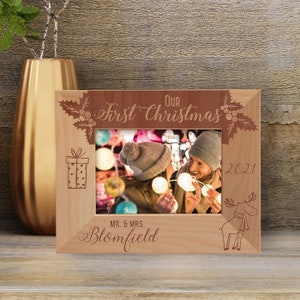 May include: A wooden photo frame with a red and brown engraved design. The frame features the text "Our First Christmas 2021" and a moose illustration. The frame also includes the text "Mr. & Mrs. Blomfield".