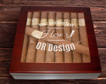 May include: A dark wood cigar humidor with a glass top lid. The glass features white printed text that reads Your Custom Text Here OR Design with a small fountain pen icon. Inside the box, several brown cigars are arranged in a row.