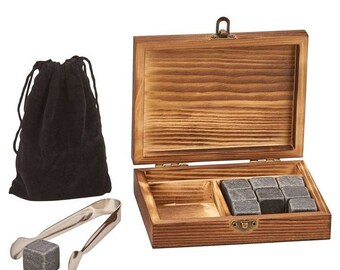 May include: A wooden box set with whiskey stones, tongs, and a black velvet bag. The box is open, revealing six gray square stones. The tongs are silver, and the bag is closed with a drawstring. A perfect gift for whiskey lovers.