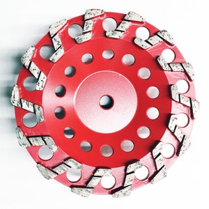 Puede incluir: Disco de esmerilado de diamante rojo con múltiples filas de segmentos de diamante alrededor del borde. El disco tiene un agujero central para montarlo en una amoladora.