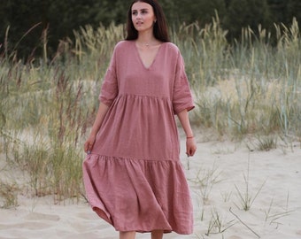Puede incluir: Un vestido midi de color rosa empolvado con escote en V, mangas hasta el codo y un diseño de falda escalonada con una costura fruncida en la cintura y un dobladillo inferior. La prenda presenta un corte holgado y relajado con un tejido texturizado.